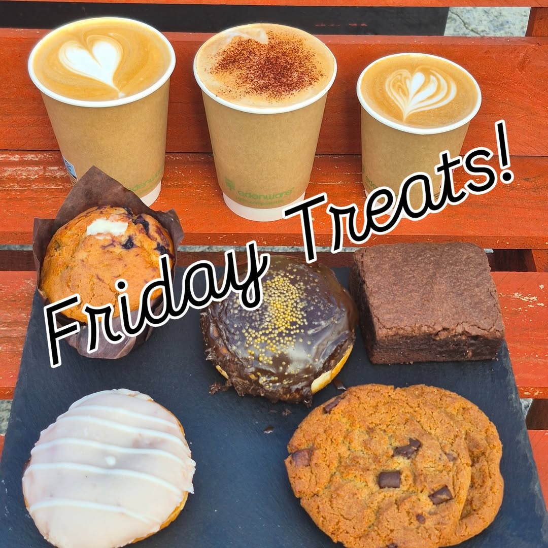Assortment of baked goods and three lattes on a wooden surface