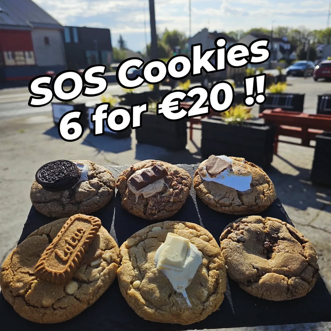 Six gourmet cookies with various toppings on a dark slate board