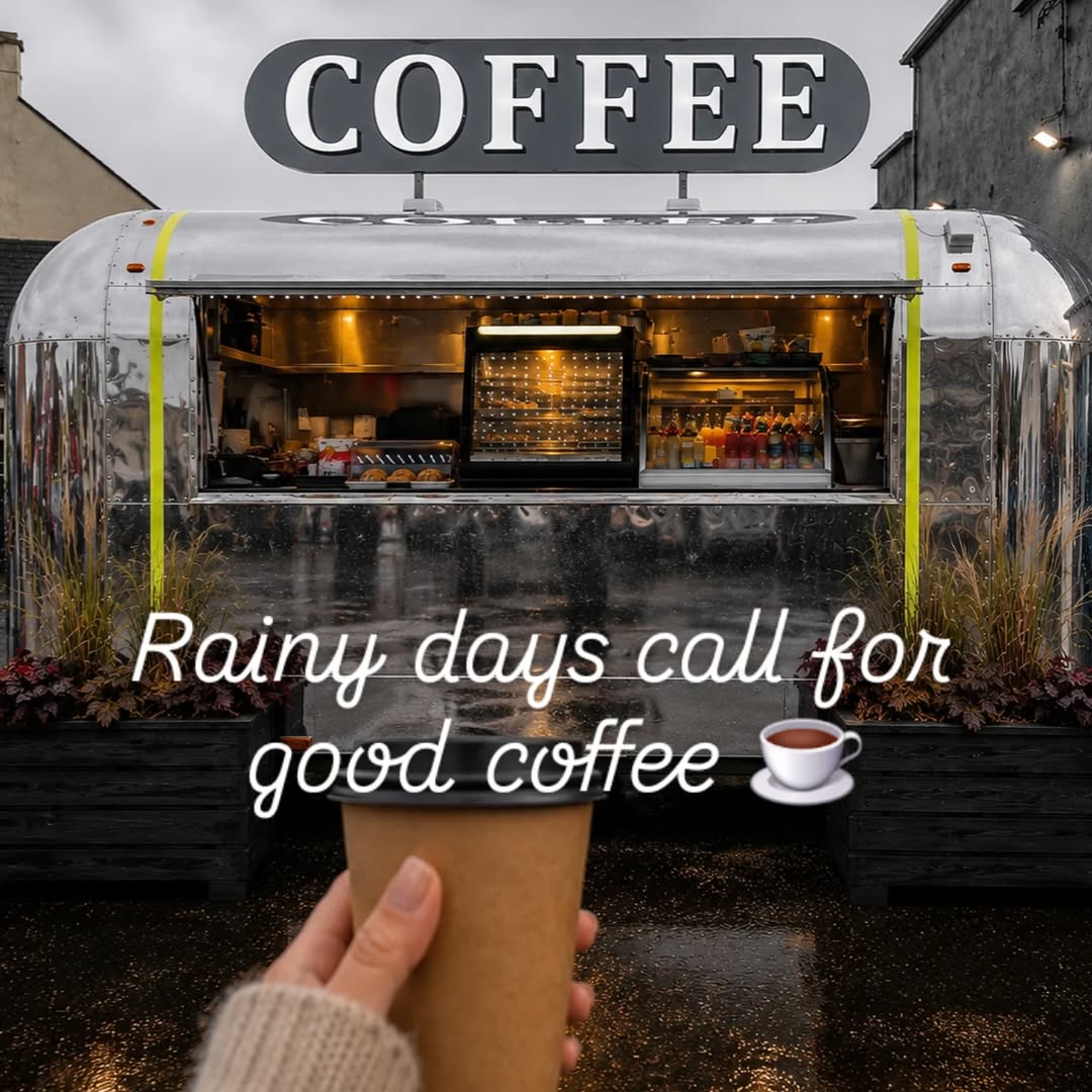 Hand holding a paper coffee cup in front of a coffee trailer on a rainy day