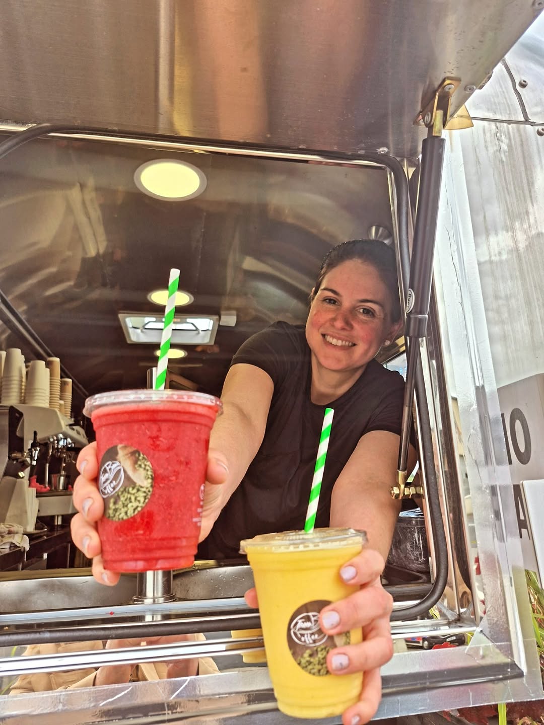 Smiling woman serving two colorful smoothies from a service window.